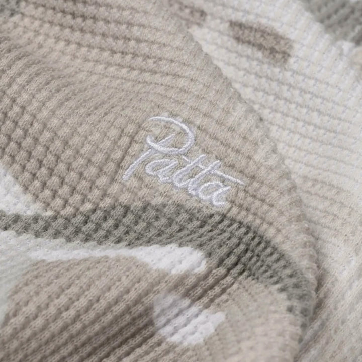 Close-up af waffle-struktur camouflageprint og Patta-branding på longsleeven
